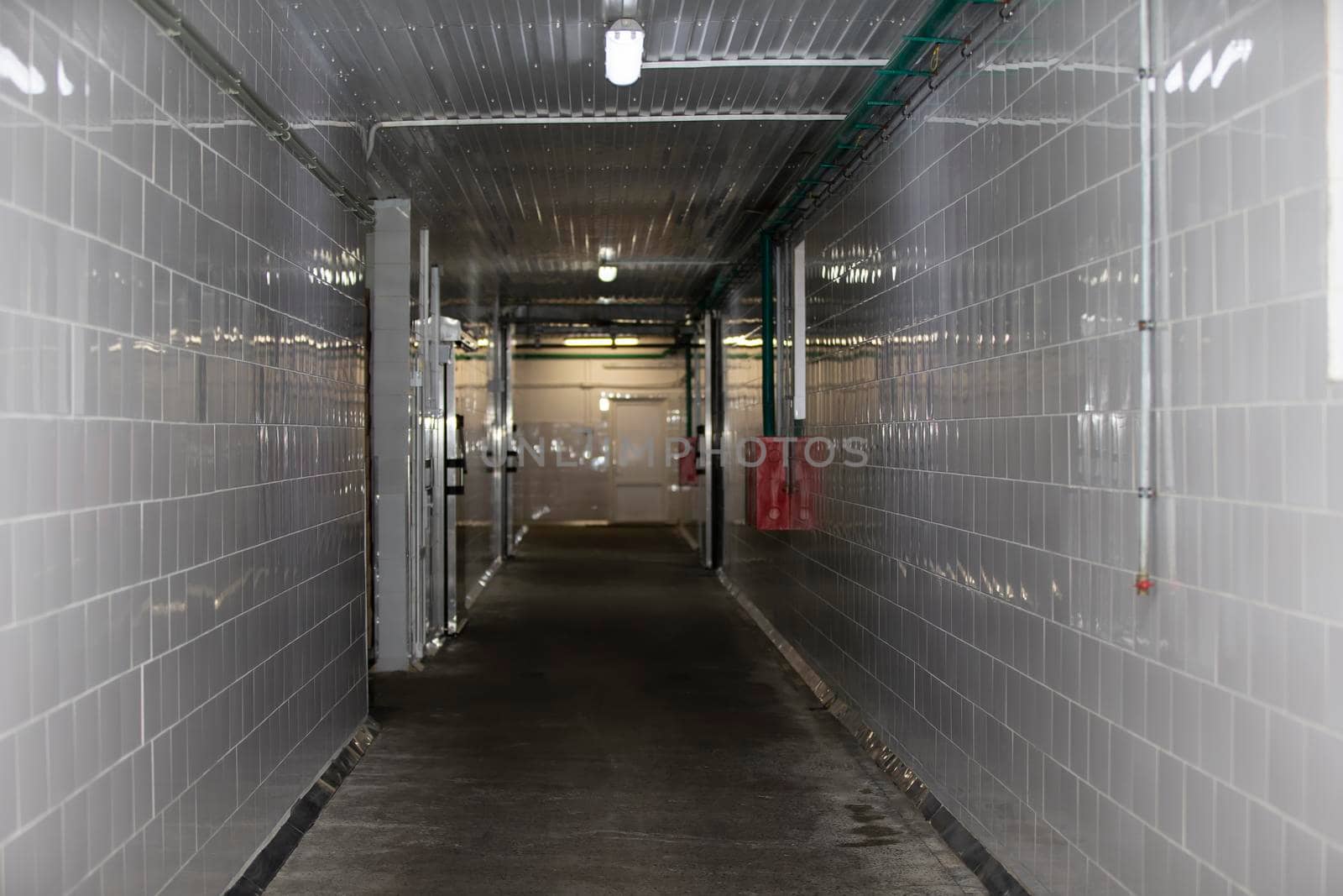 An empty corridor of a factory or workshop is faced with tiles and concrete floor.