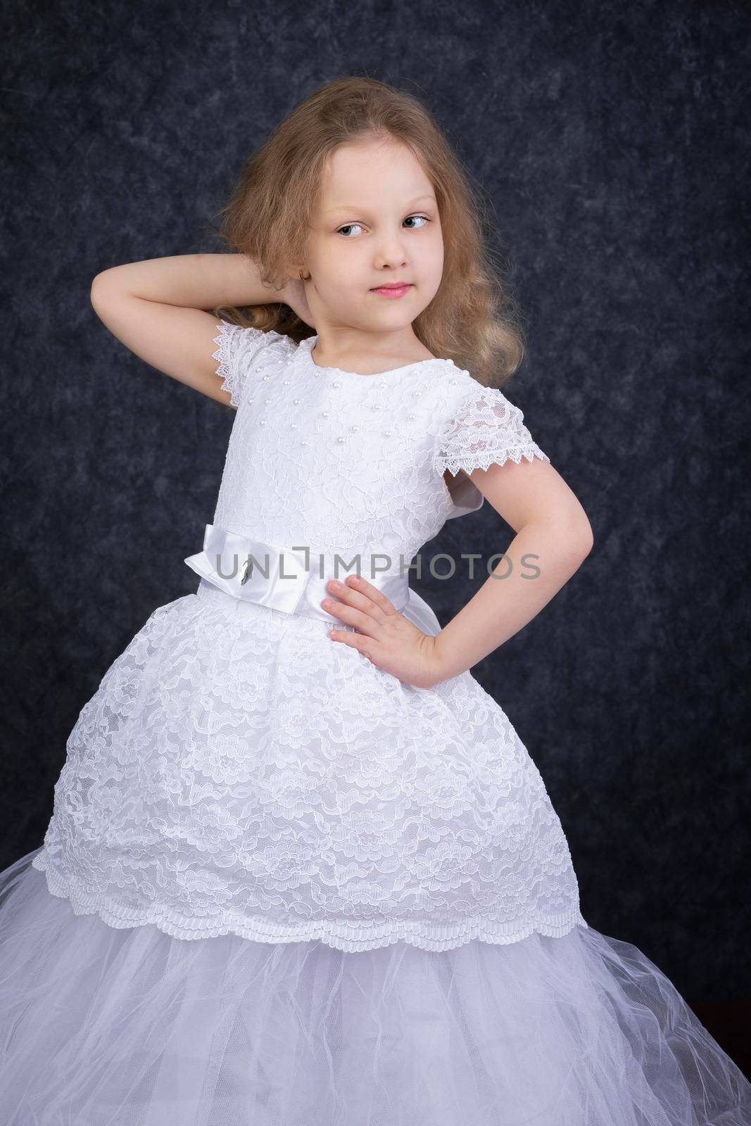 Cute little blonde girl in a beautiful white dress on a dark background. Six year old beautiful girl
