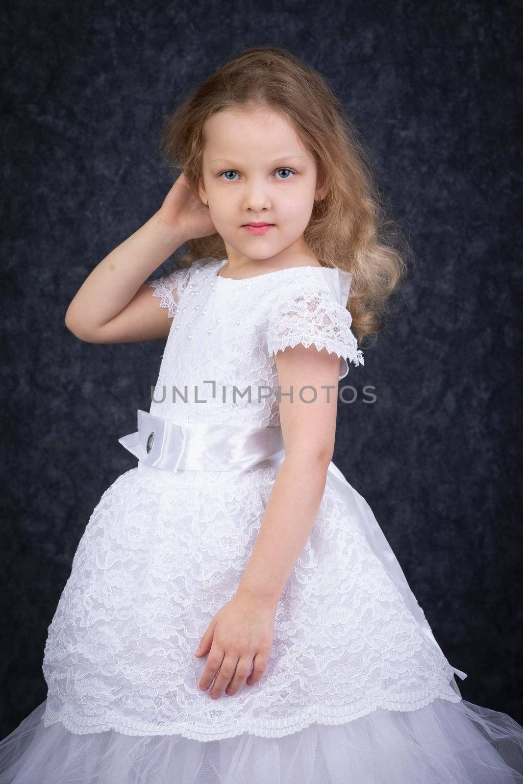 Cute little blonde girl in a beautiful white dress on a dark background. Six year old beautiful girl