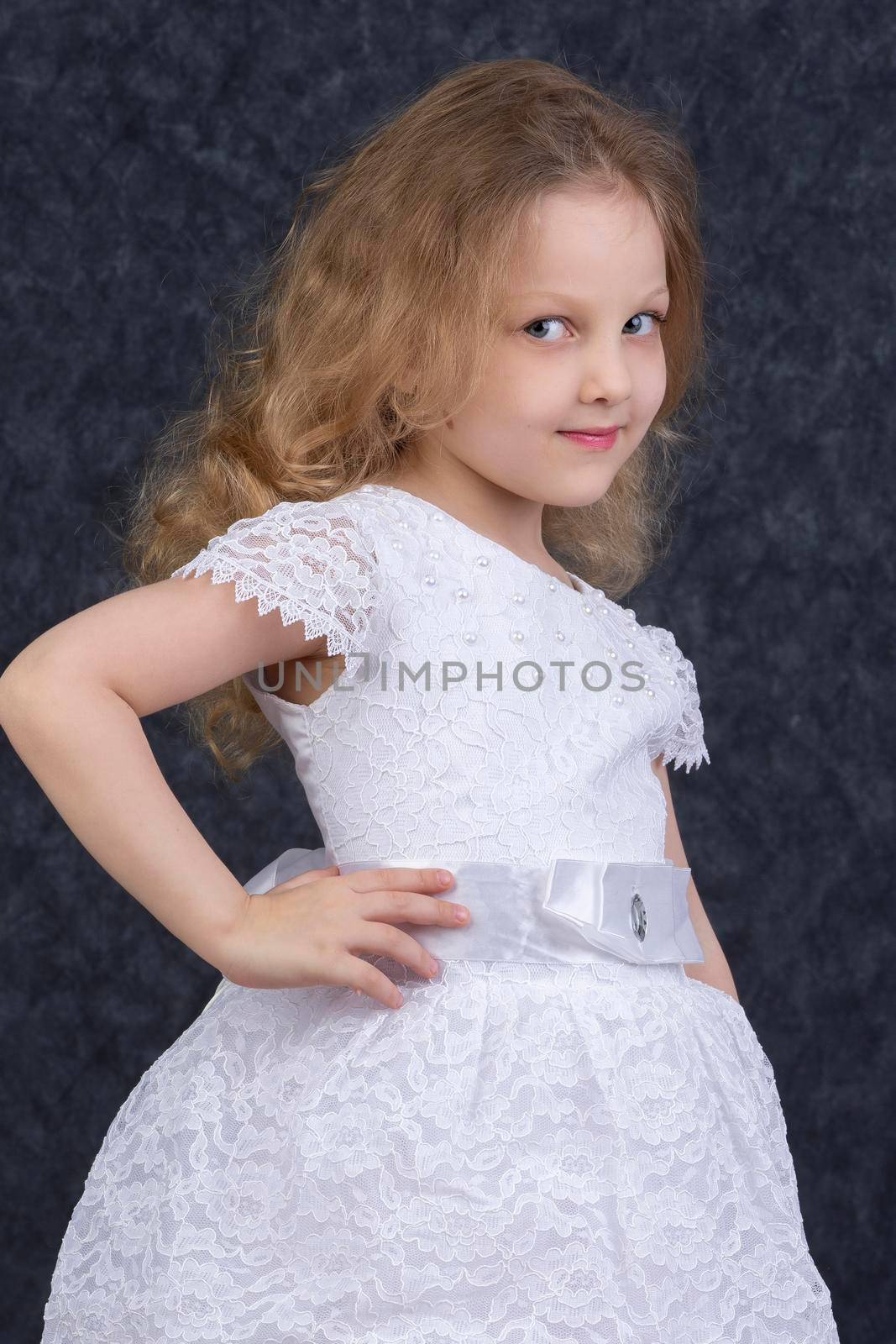 Cute little blonde girl in a beautiful white dress on a dark background. Six year old beautiful girl