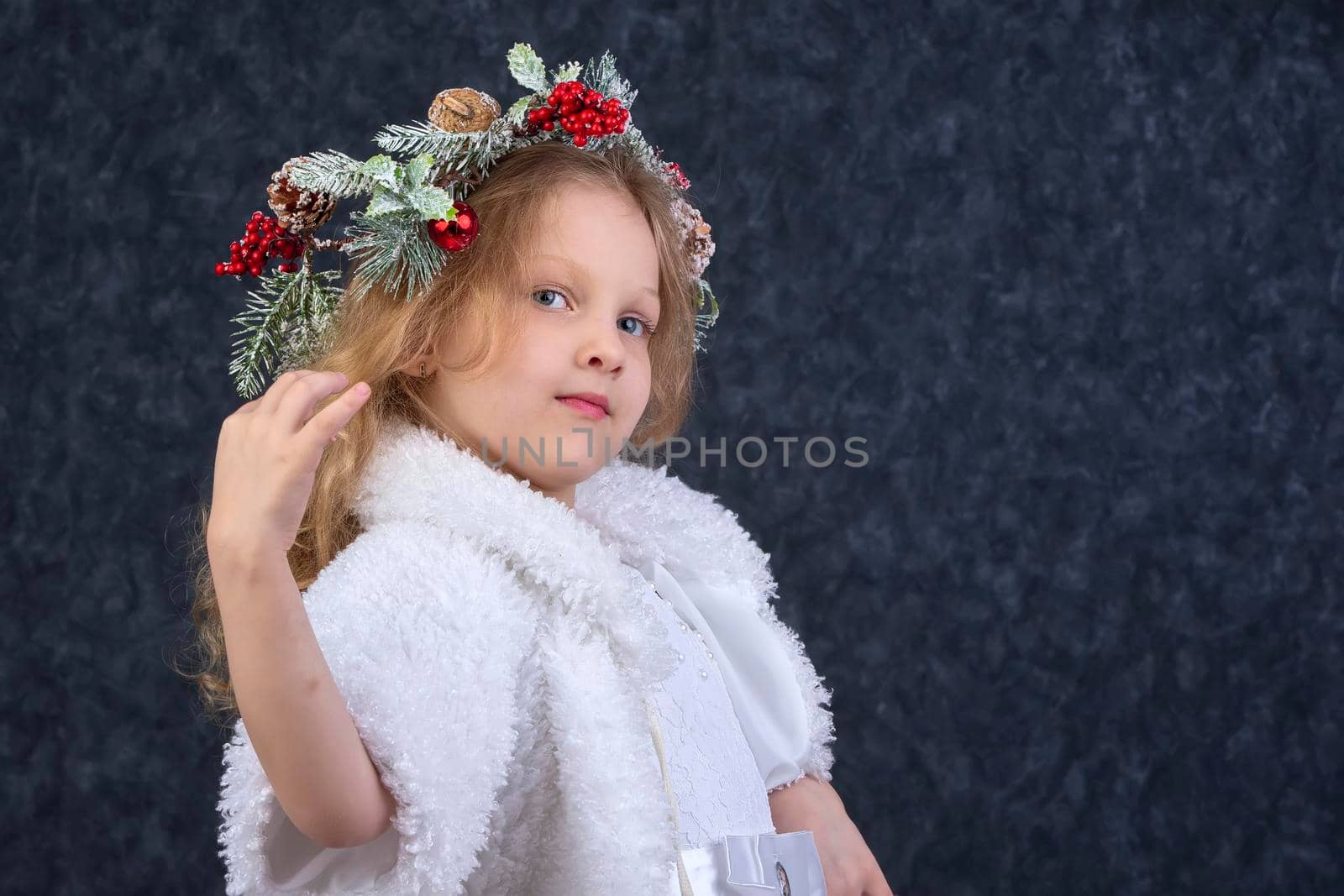 Beautiful little girl in a white dress with a Christmas wreath on her head. Christmas child.