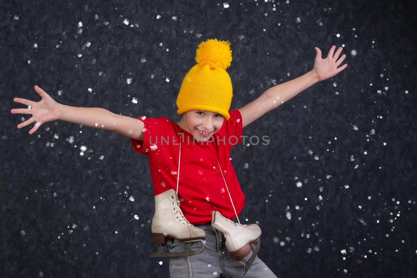 Handsome little boy in a knitted yellow hat with vintage skates on a gray background.