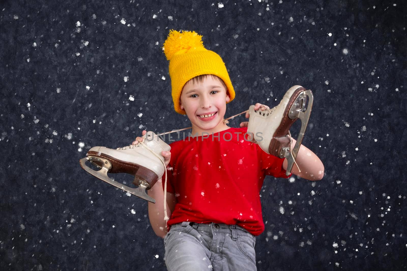 Handsome little boy in a knitted yellow hat with vintage skates on a gray background.