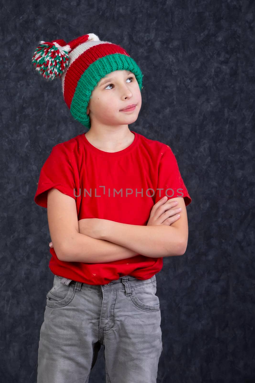 Funny little boy in a knitted Christmas hat on a gray background.