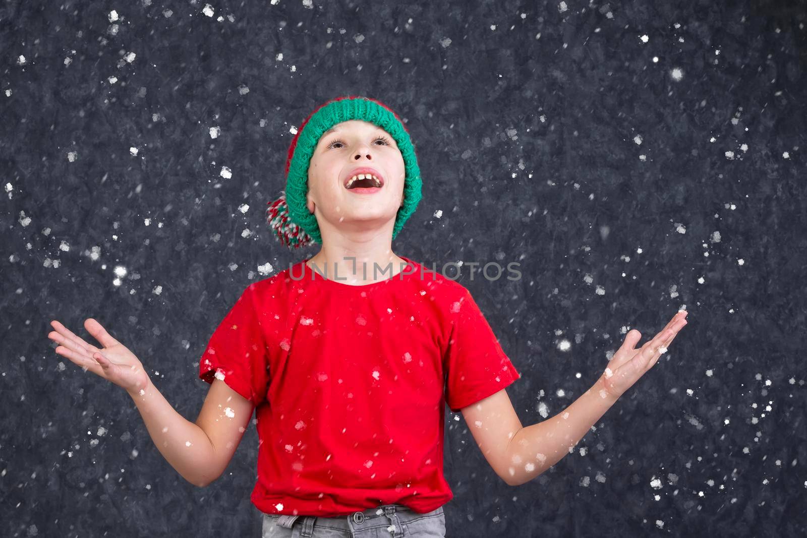 A funny little boy in a red T-shirt catches the flying snow.