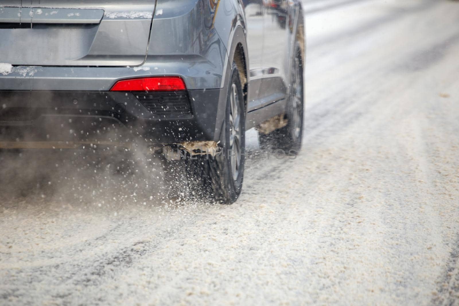 Road snow flinders flow from wheels of gray car moving fast in daylight city with selective focus. by z1b