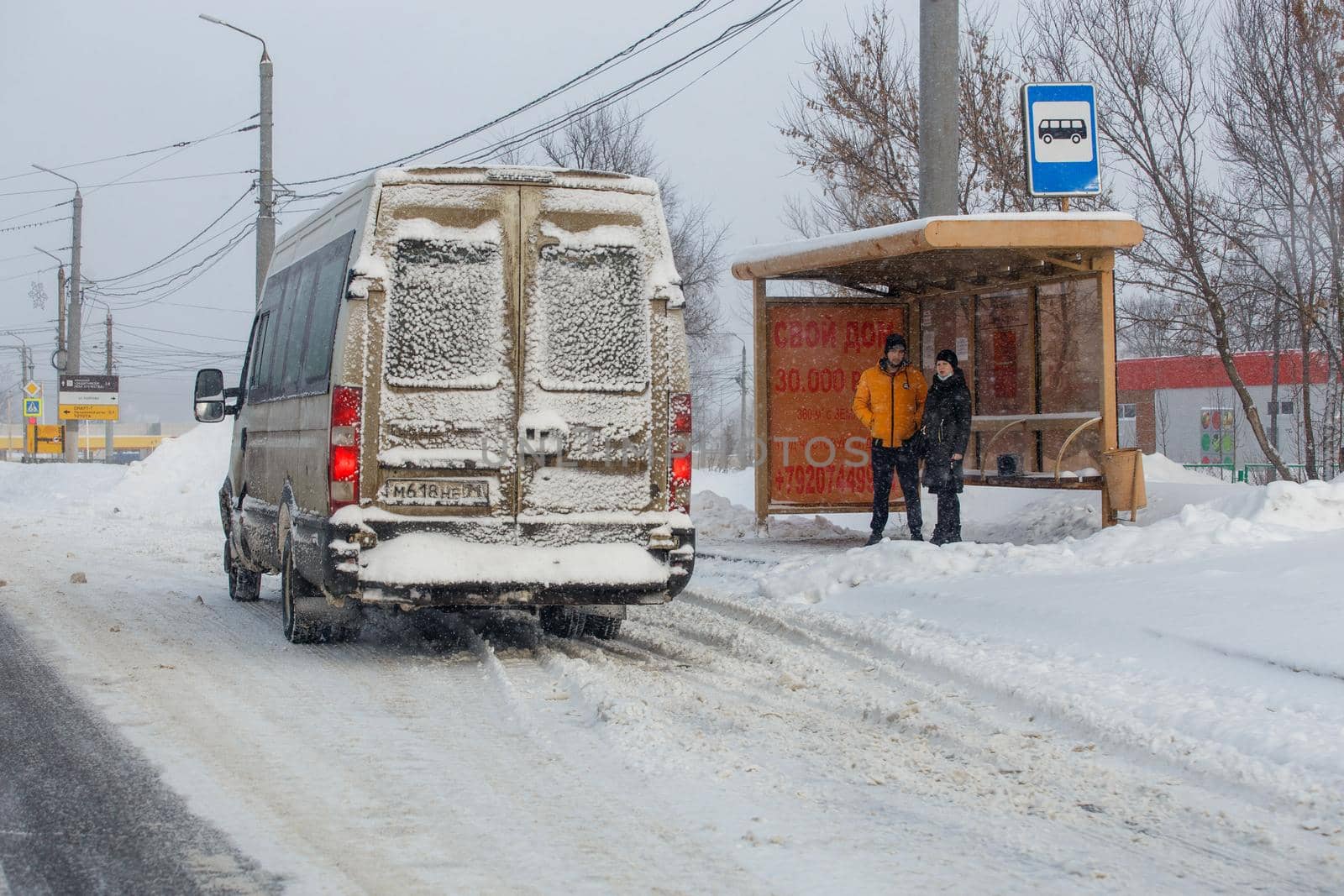 Tula, Russia - February 13, 2021: Man and woman waiting transport on bus stop at winter snowy day