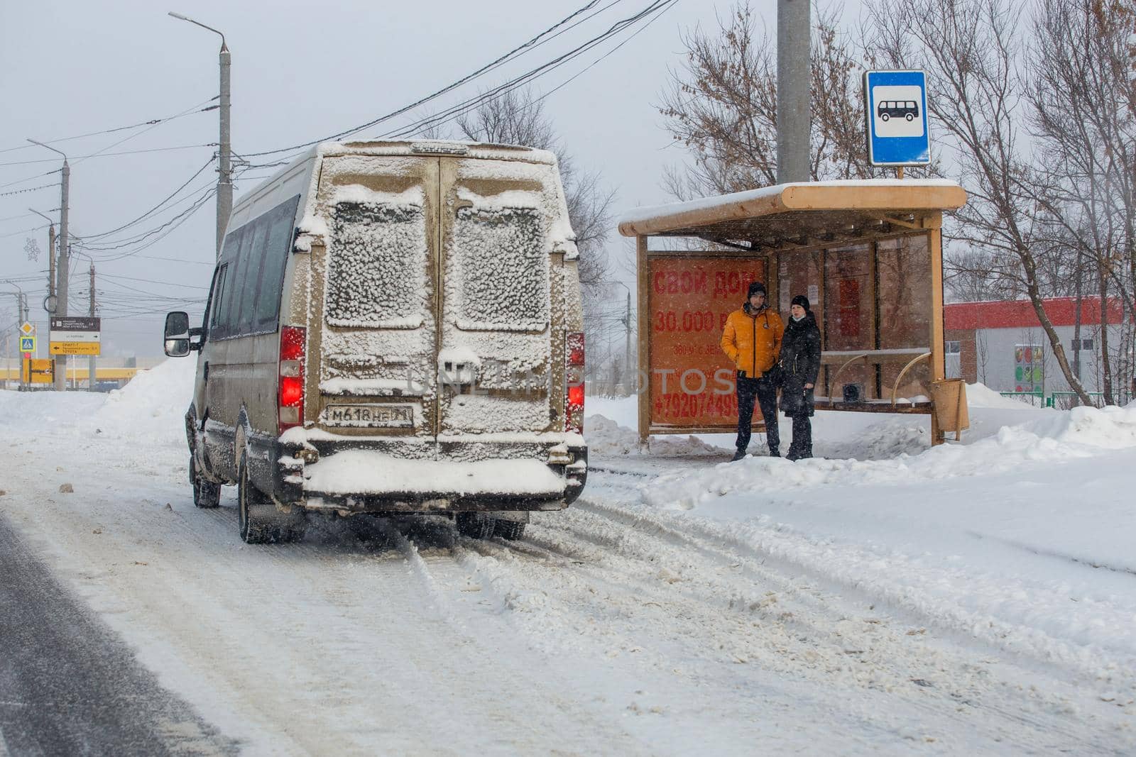 Man and woman waiting transport on bus stop at winter snowy day in Tula, Russia by z1b