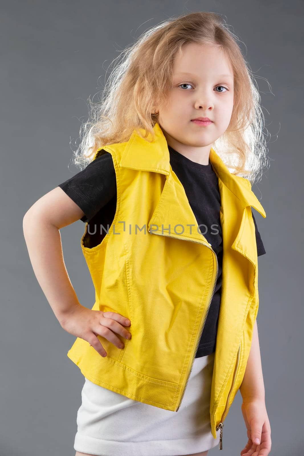 Beautiful little blonde girl in a yellow jacket on a gray background. Five year old girl. Model tests for a child.