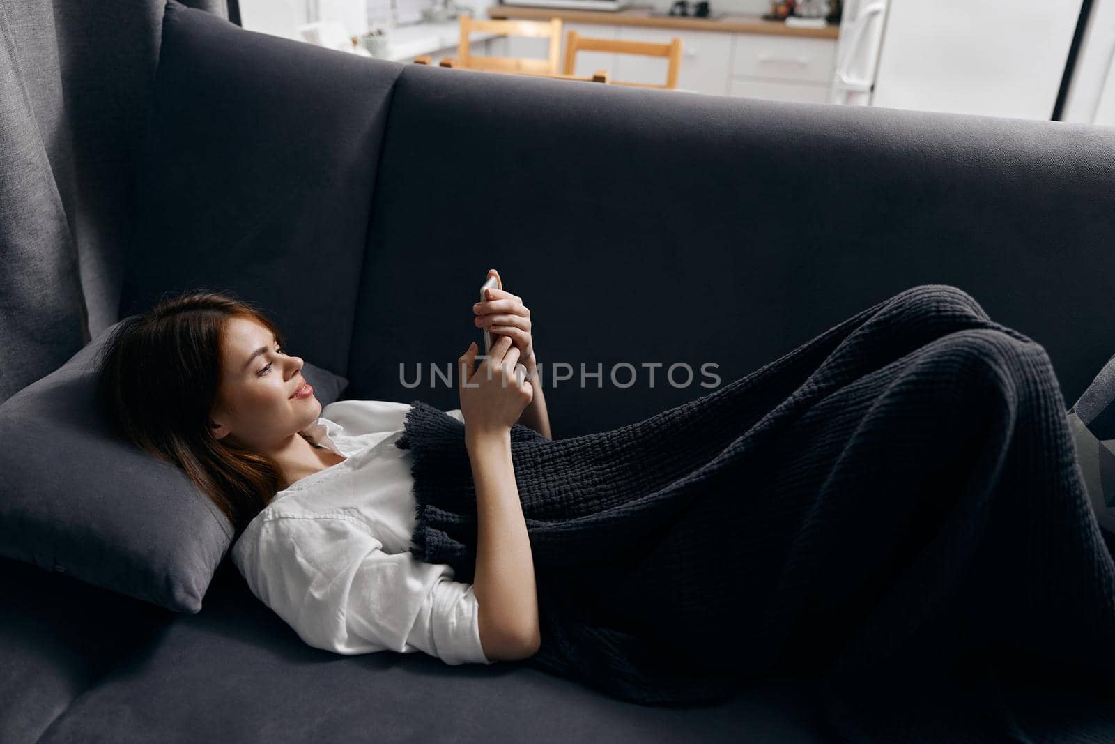 woman resting on the couch with a phone in her hand and a gray plaid on her legs by SHOTPRIME