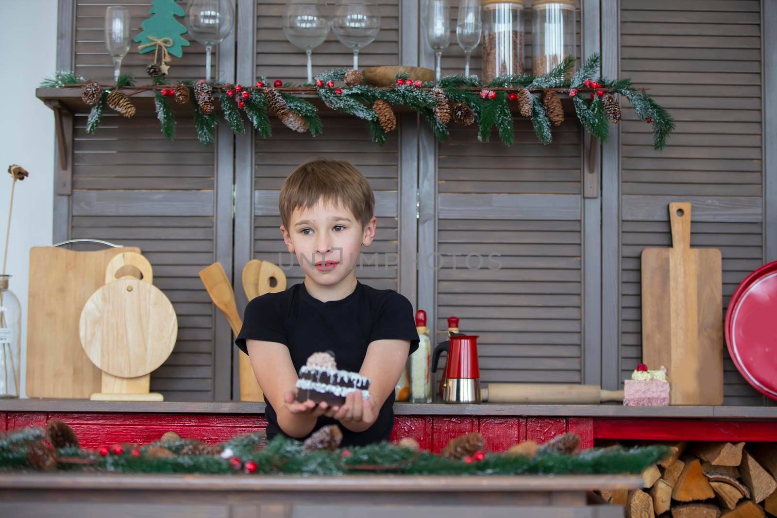 A boy in the Christmas kitchen at home holds a cake in his hands.