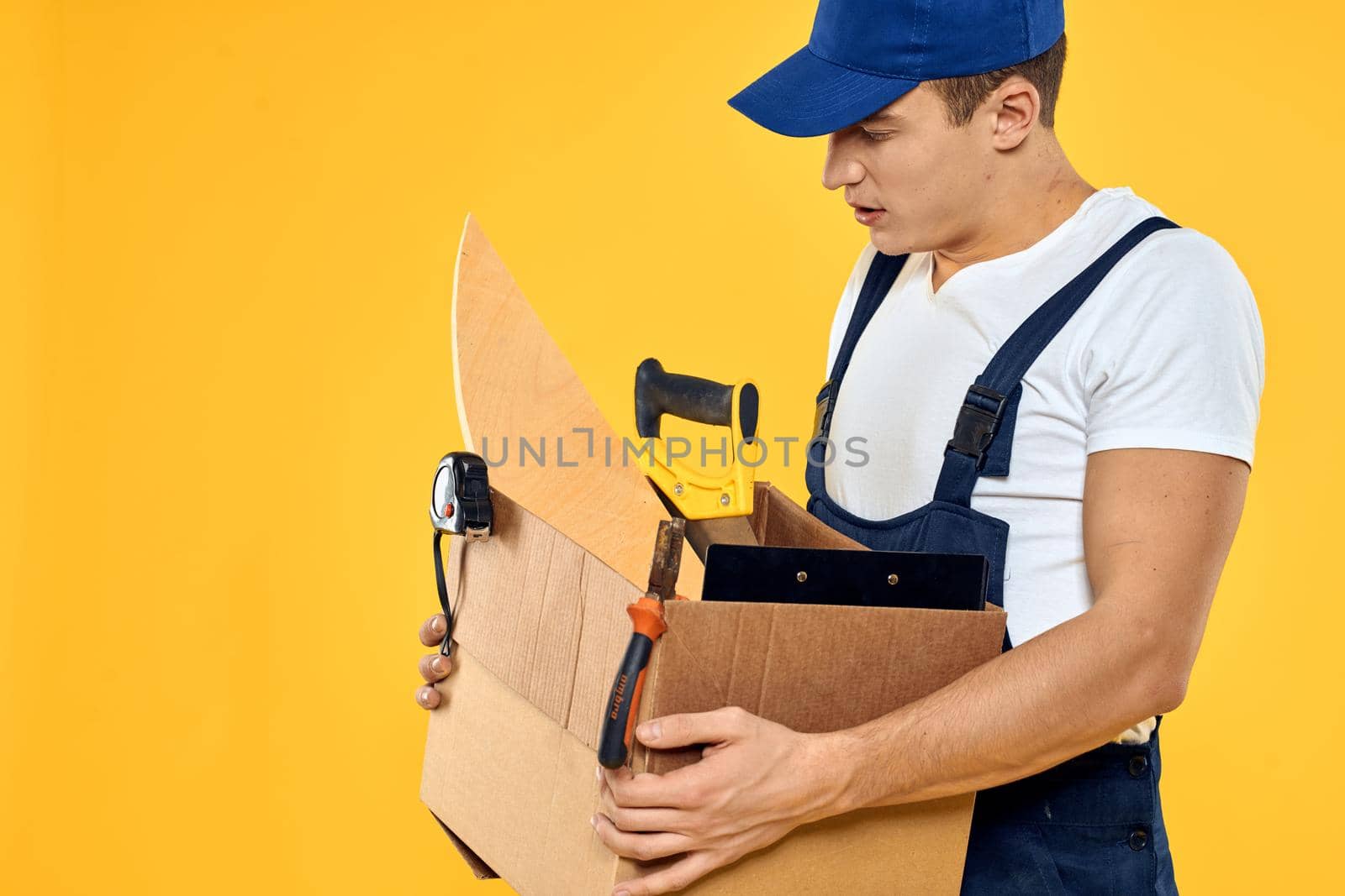 A man with a box in his hands working uniform that delivery service yellow background. High quality photo