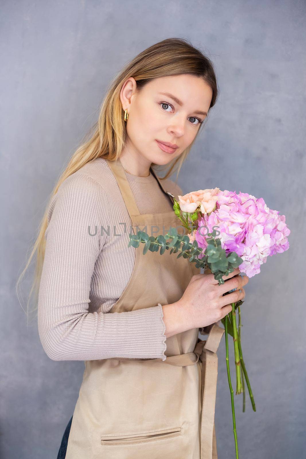 Young caucasian female florist collects a romantic bouquet of roses. People in the process of work. The concept of a flower shop and flower delivery as a family business.