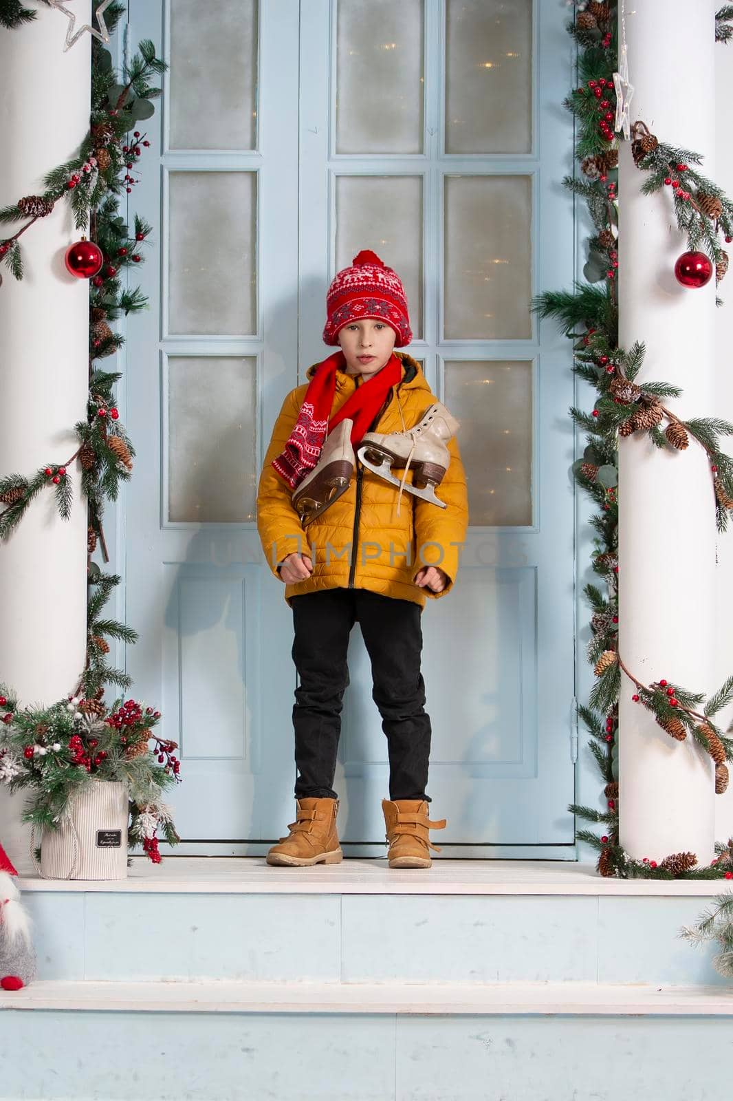 Handsome little boy in christmas. Funny child on the porch of the Christmas house in bright clothes with old skates.