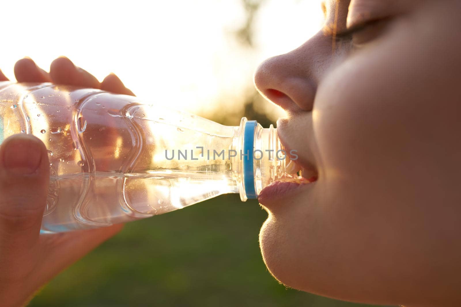 woman drinks water from a plastic bottle outdoors in summer close-up by SHOTPRIME