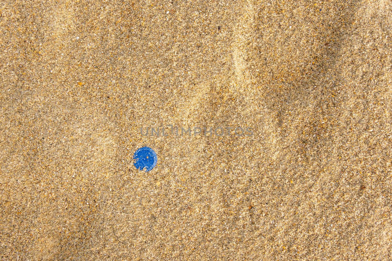 Blue water bottle cap in beach sand, plastic pollution concept