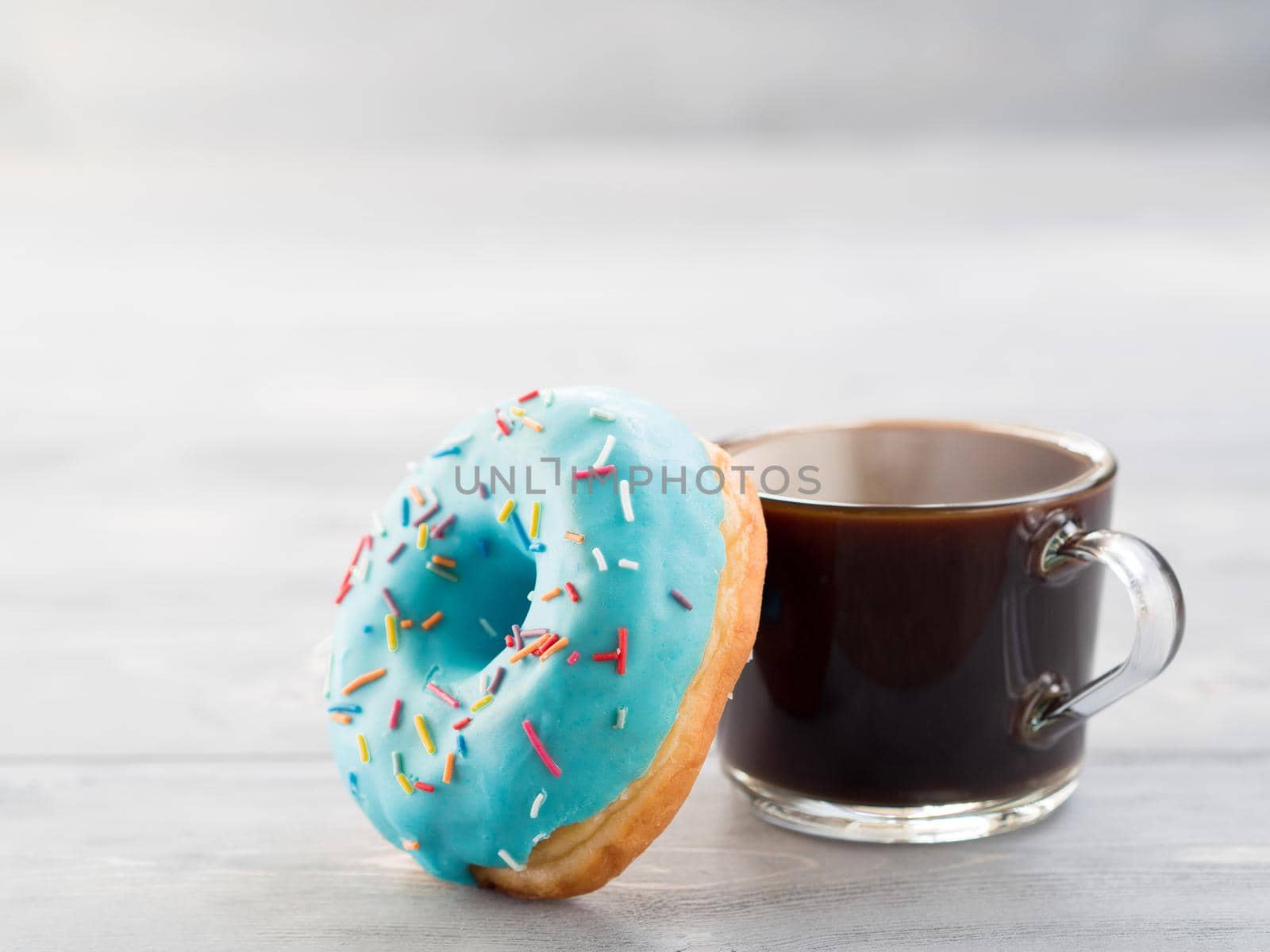 Blue donut and coffee on gray wooden background with copy space. Glazed doughnut and coffee cup on grey wooden table with copyspace