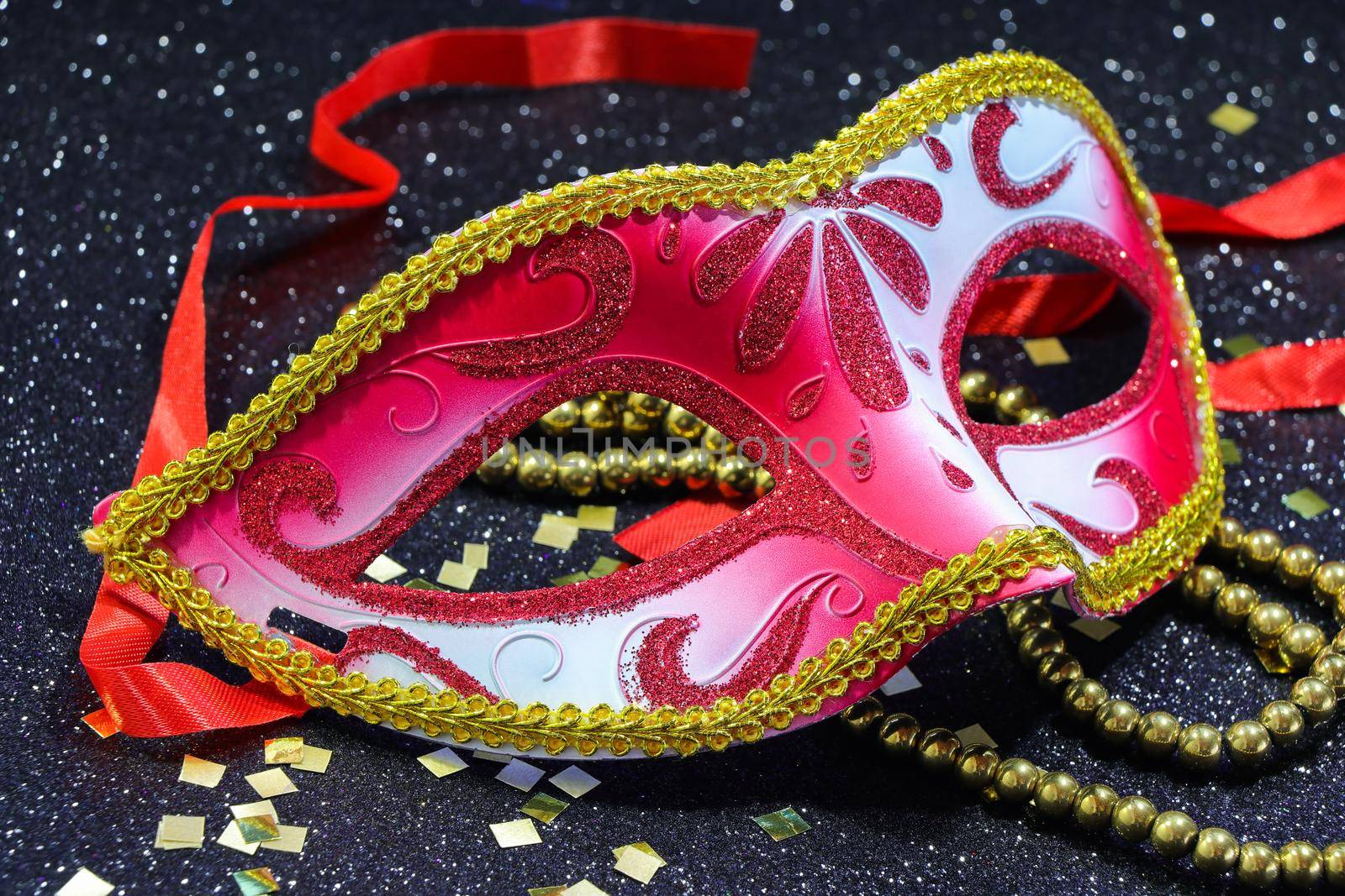 Mardi Gras red carnival face mask with gold bead string and confetti on textured black