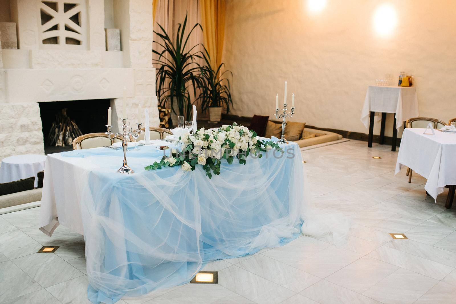 the presidium of the newlyweds in the banquet hall of the restaurant is decorated with candles and green plants, the general tone of the hall is beige by Andreua