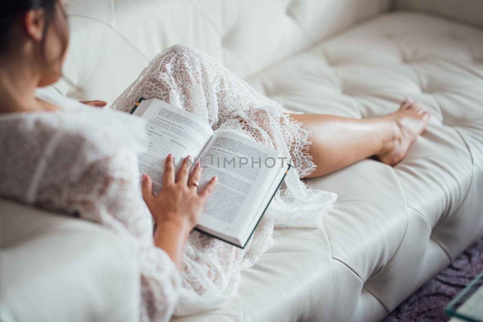 girl with black hair reads a book in Russian sitting on a light leather sofa
