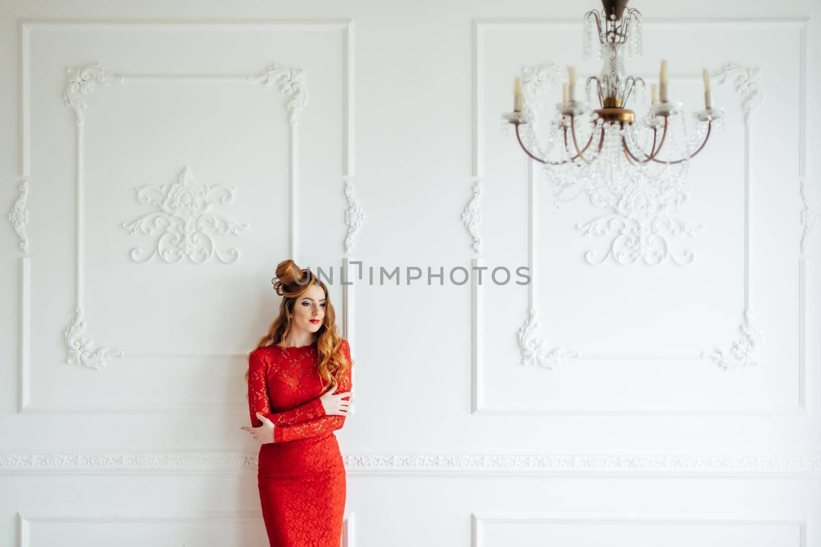 young girl with red hair in a bright red dress in a light room near a white wall