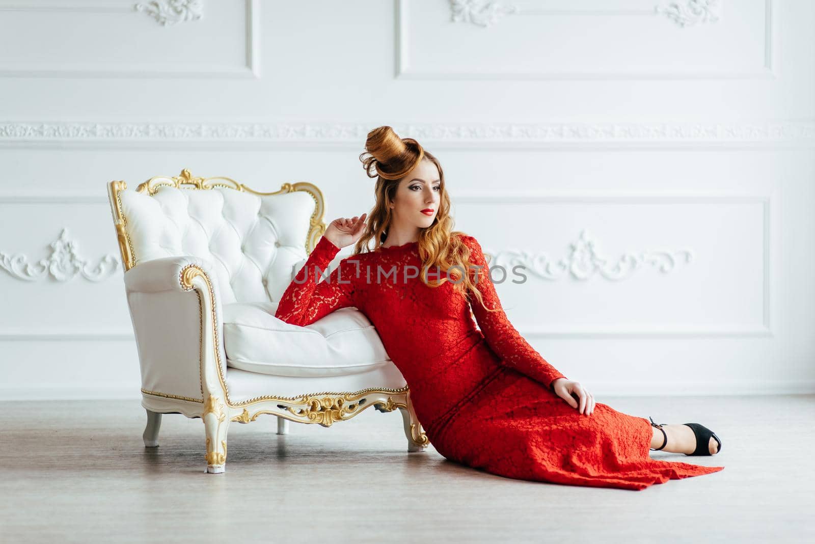 young girl with red hair in a bright red dress in a bright room on an antique sofa