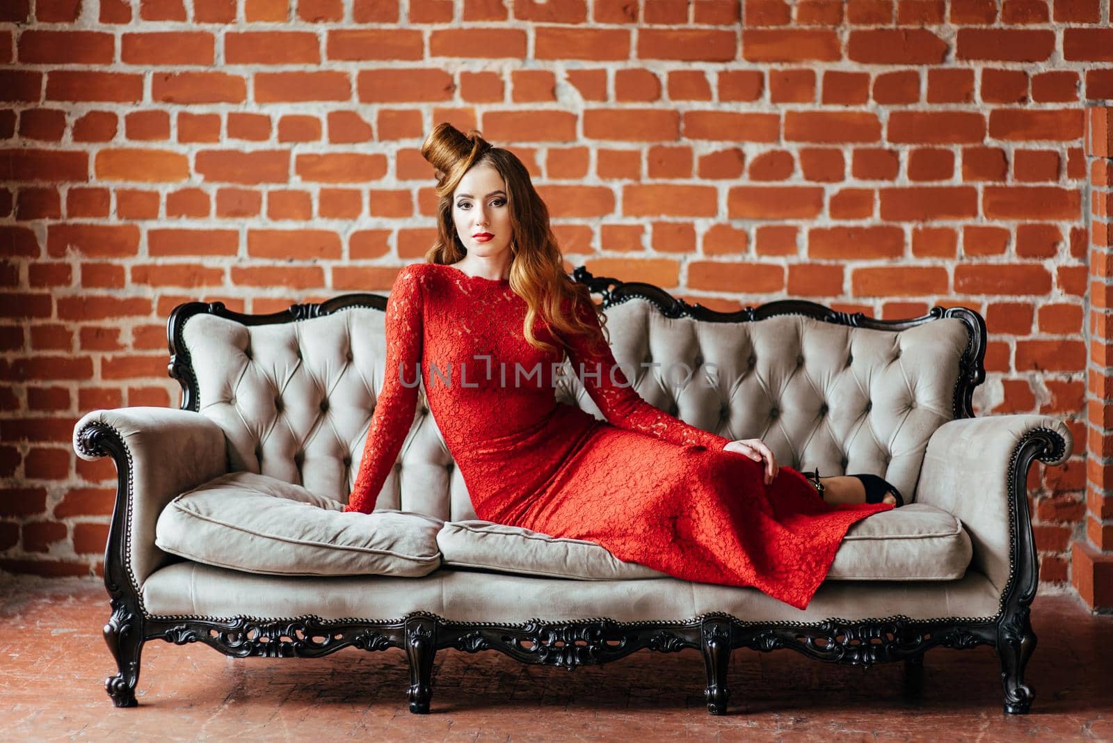 young girl with red hair in a bright red dress in a bright room on an antique sofa