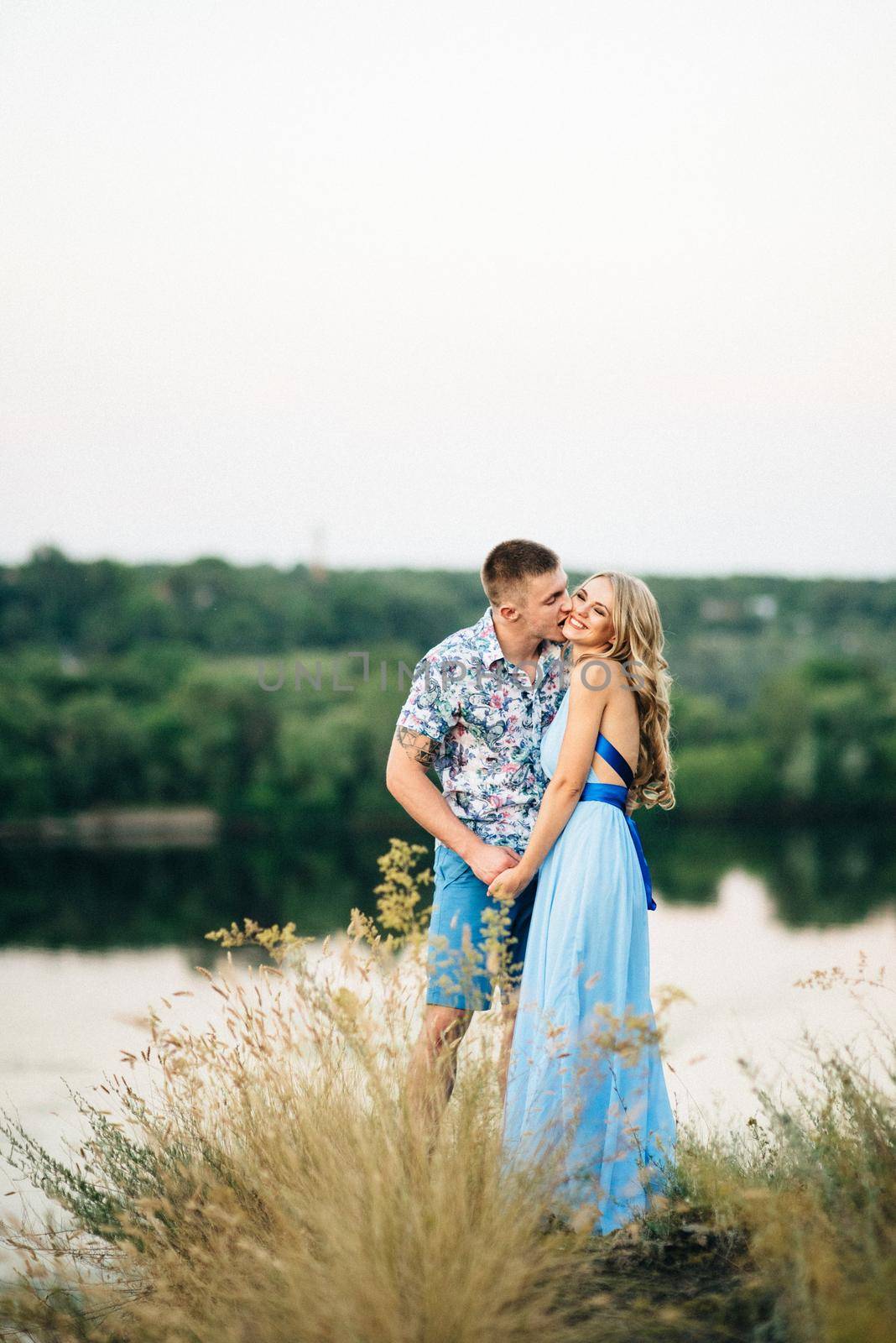 blonde girl with loose hair in a light blue dress and a guy in the light of sunset in nature