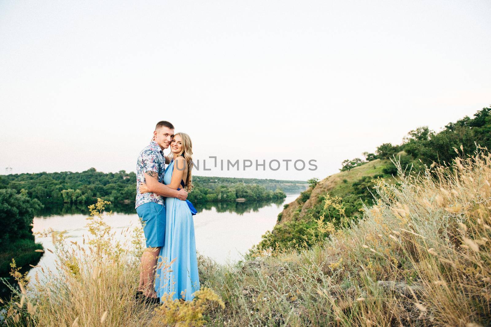 blonde girl with loose hair in a light blue dress and a guy in the light of sunset in nature