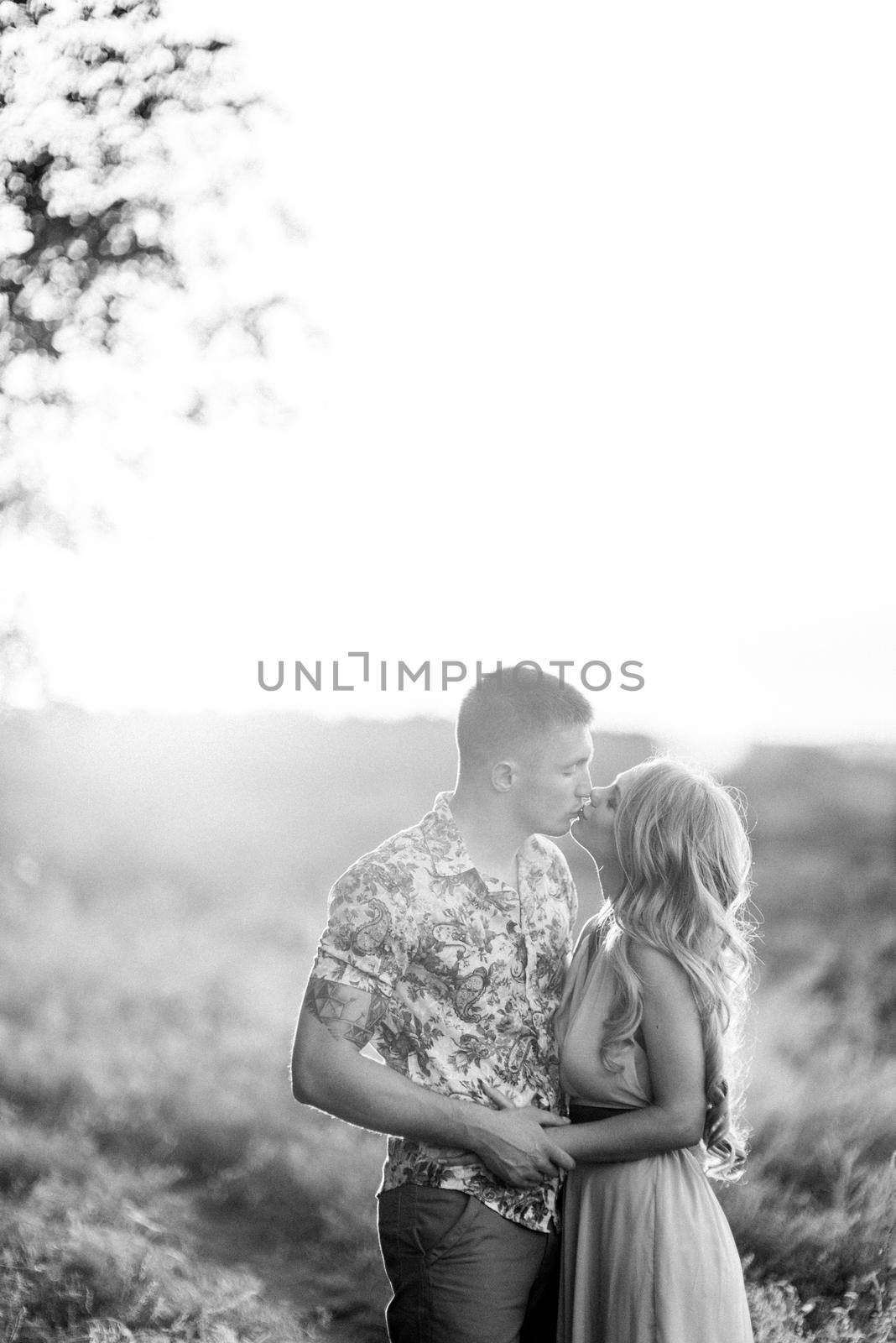 blonde girl with loose hair in a light blue dress and a guy in the light of sunset in nature