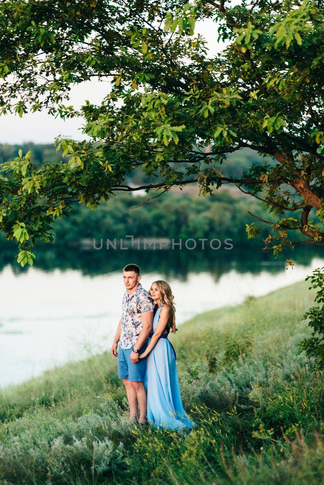 blonde girl with loose hair in a light blue dress and a guy in the light of sunset in nature