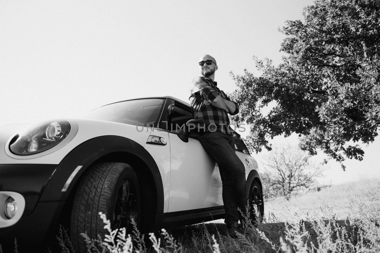 Guy in a plaid shirt next to a white car in nature