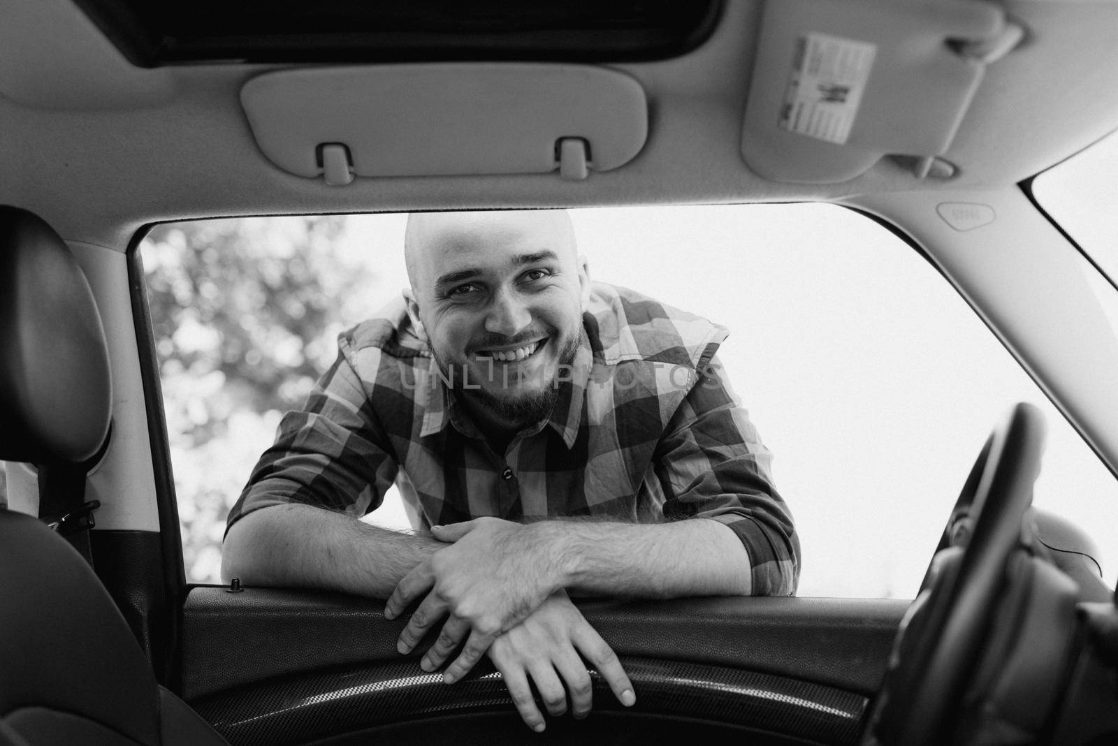 Guy in a plaid shirt next to a white car in nature