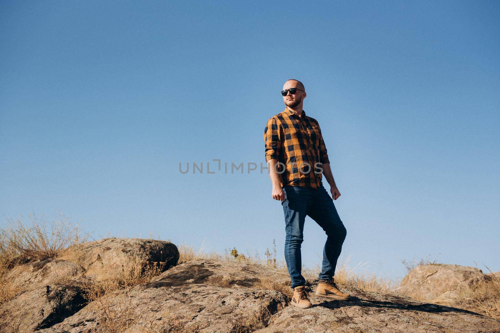 bald guy with a beard in jeans warm shirt and trekking shoes on granite rocks