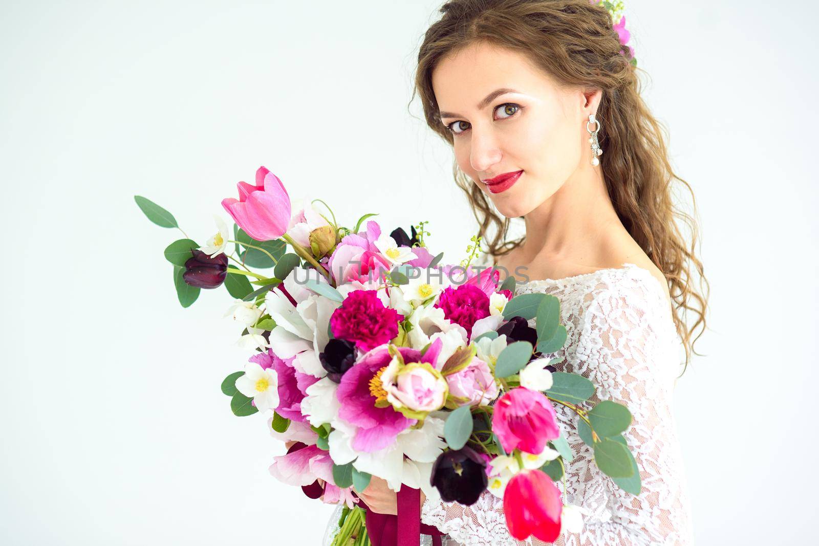 joyful girl bride in a white knitted dress posing with a bouquet of flowers in the studio on a white background