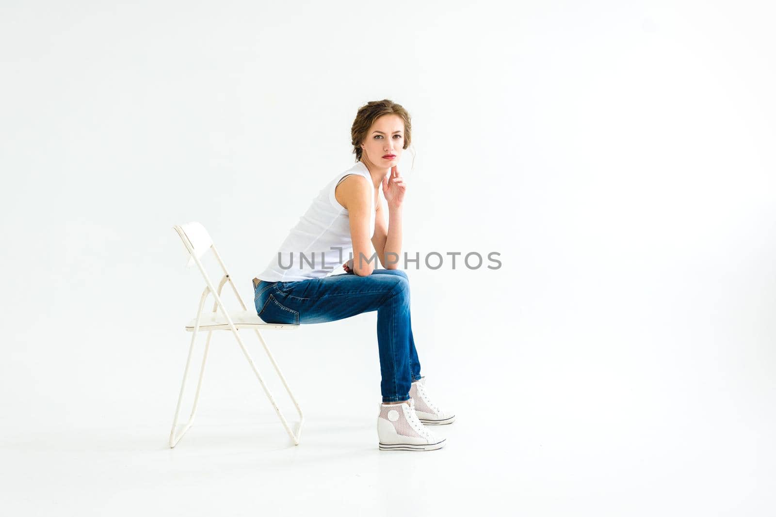 cheerful girl in a white t-shirt and dark blue jeans in the studio on a white background stands, sits, runs