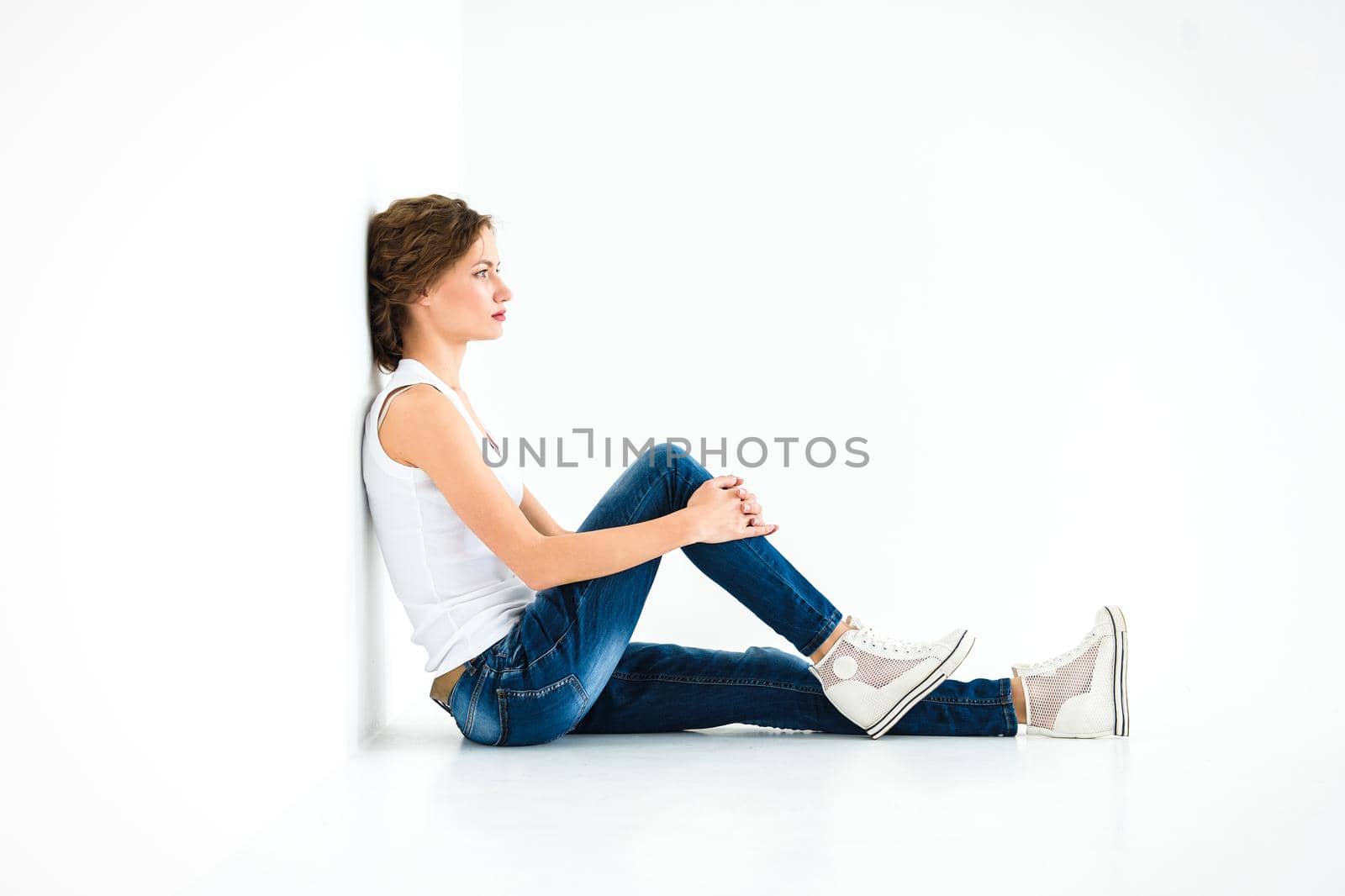 cheerful girl in a white t-shirt and dark blue jeans in the studio on a white background stands, sits, runs