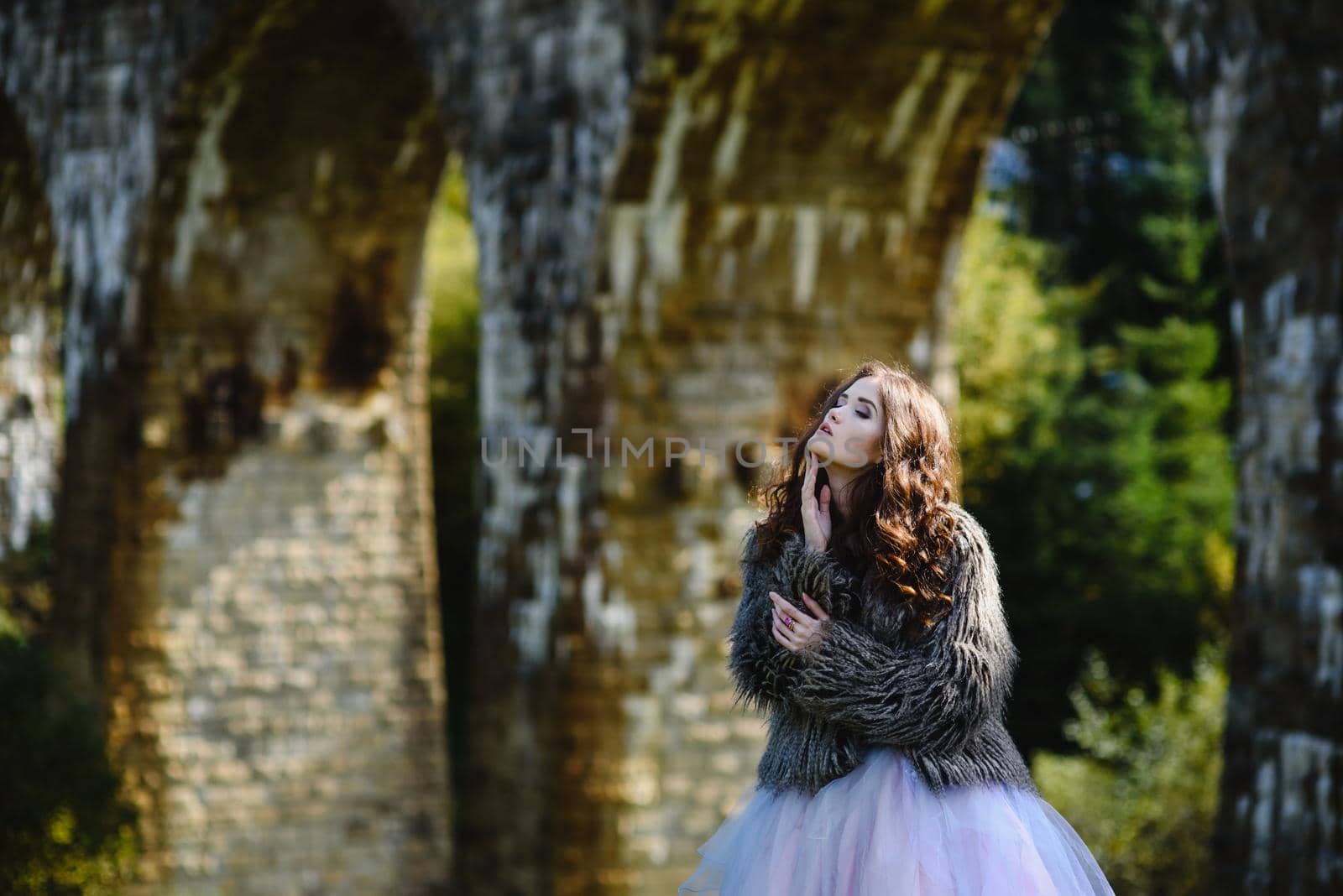 the bride walks under a bridge in a fur Cape in the Carpathians