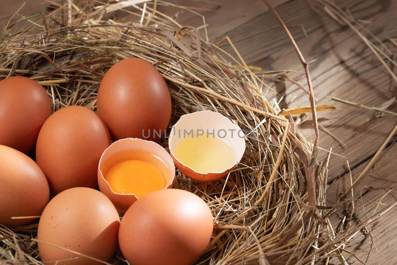 Several raw fresh chicken eggs in a nest of hay on a wooden background by galsand
