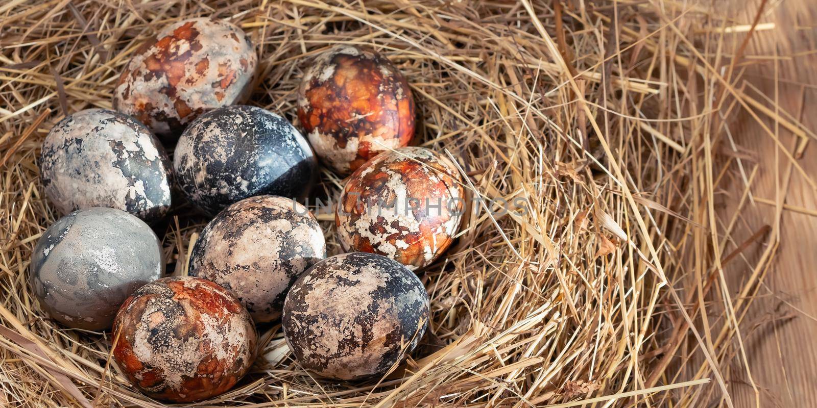 Easter composition - multicolored marble Easter eggs painted with natural dyes in a nest of hay, horizontal banner.