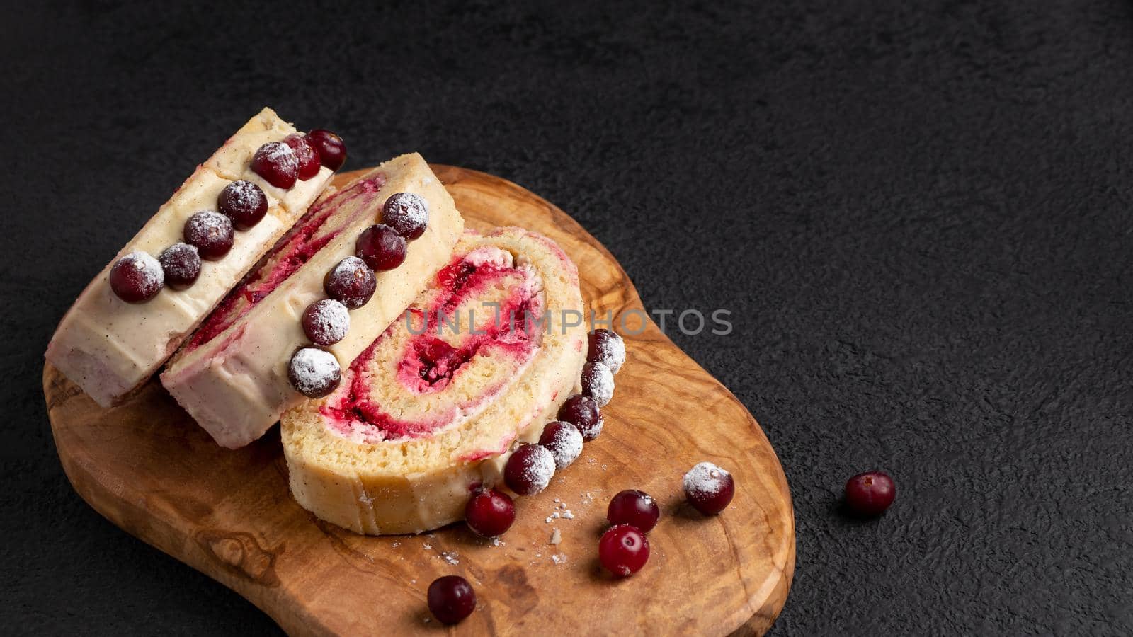 Homemade biscuit sweet roll with cranberries and cream on a black table, copy space.