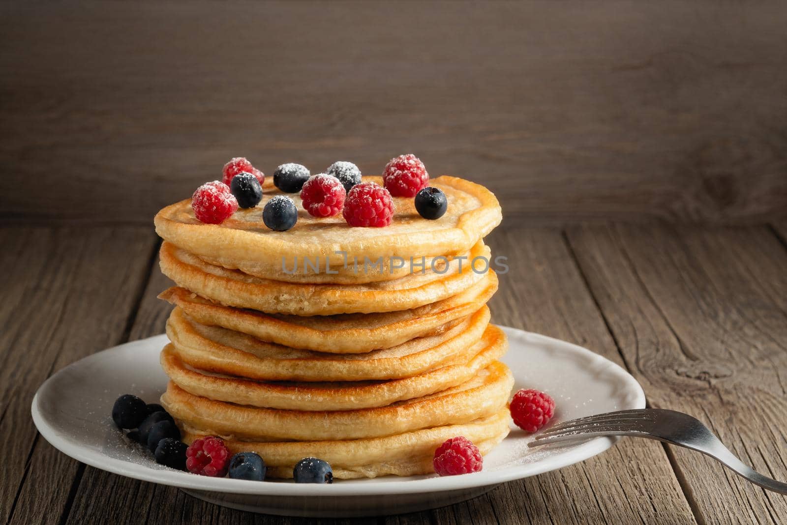 Stack of pancakes with fresh berries on a white plate on the table, copy space by galsand