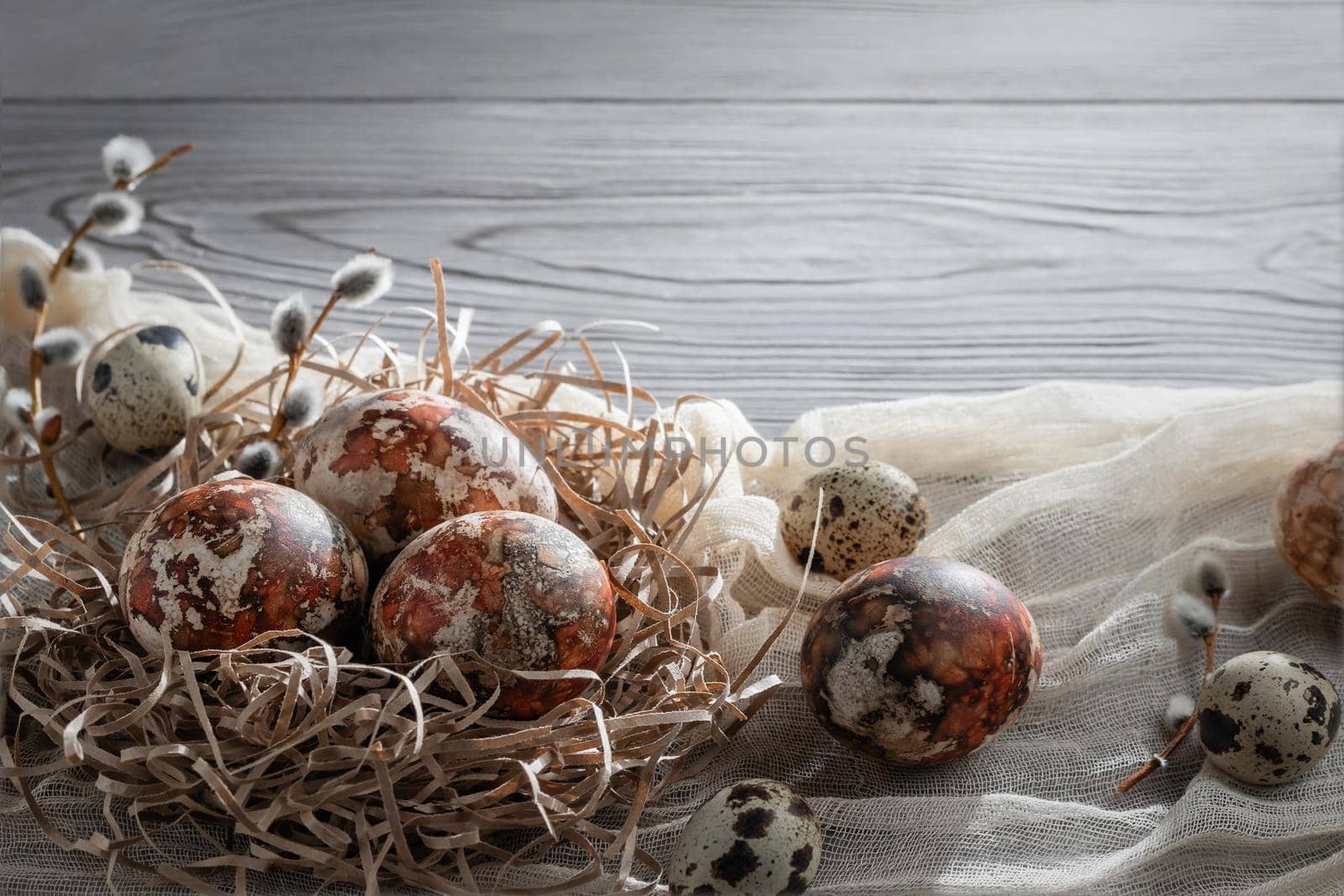 Easter composition - several marble eggs painted with natural dyes in a paper nest on the table, copy space by galsand