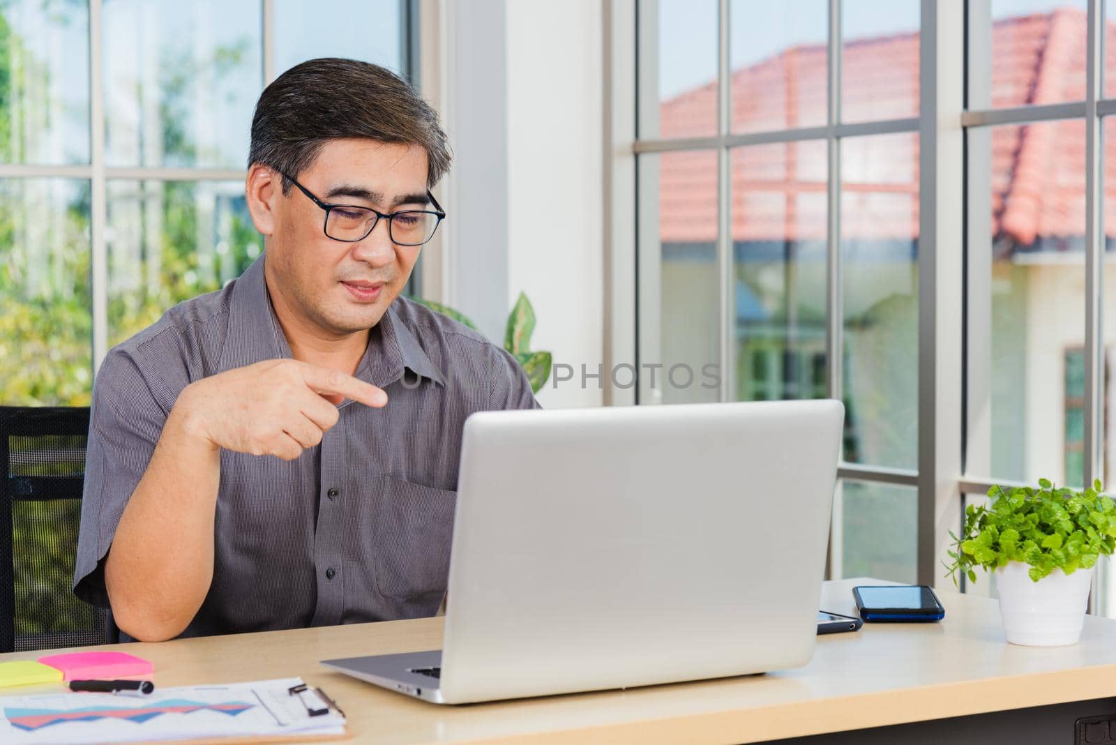 Asian senior business man working online on a modern laptop computer he looking at the screen for remote online studying. Old businessman people using the laptop to video call conference on desk table