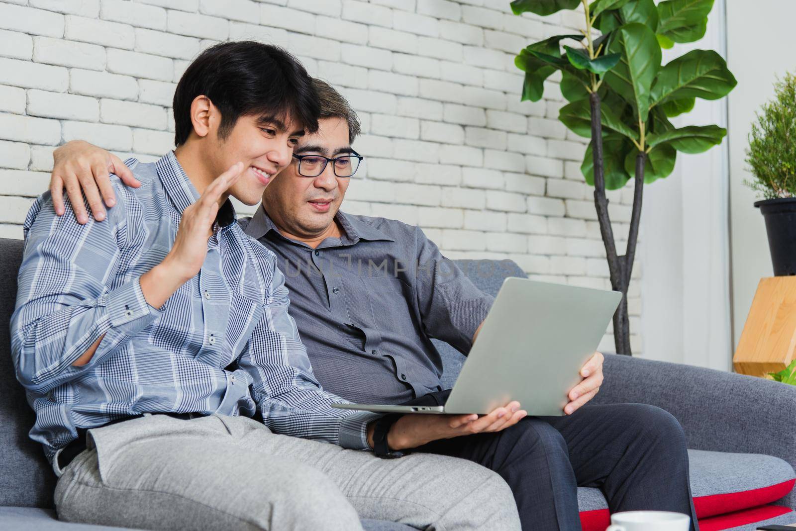 Father man and his son sit on sofa talking chatting on video call by Sorapop