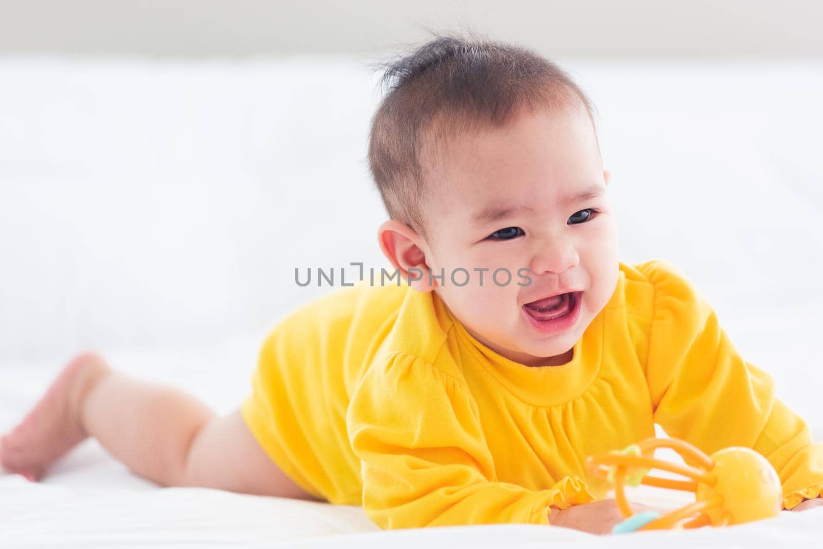 Portrait of beautiful young Asian newborn little baby prone on the bed at home, Happy baby smile wears a yellow shirt relaxing in the room, Family morning at home