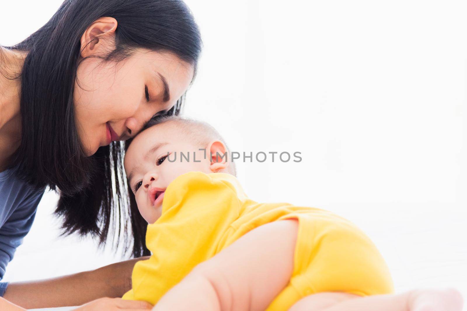 mother kissing her infant newborn baby in a white bed by Sorapop