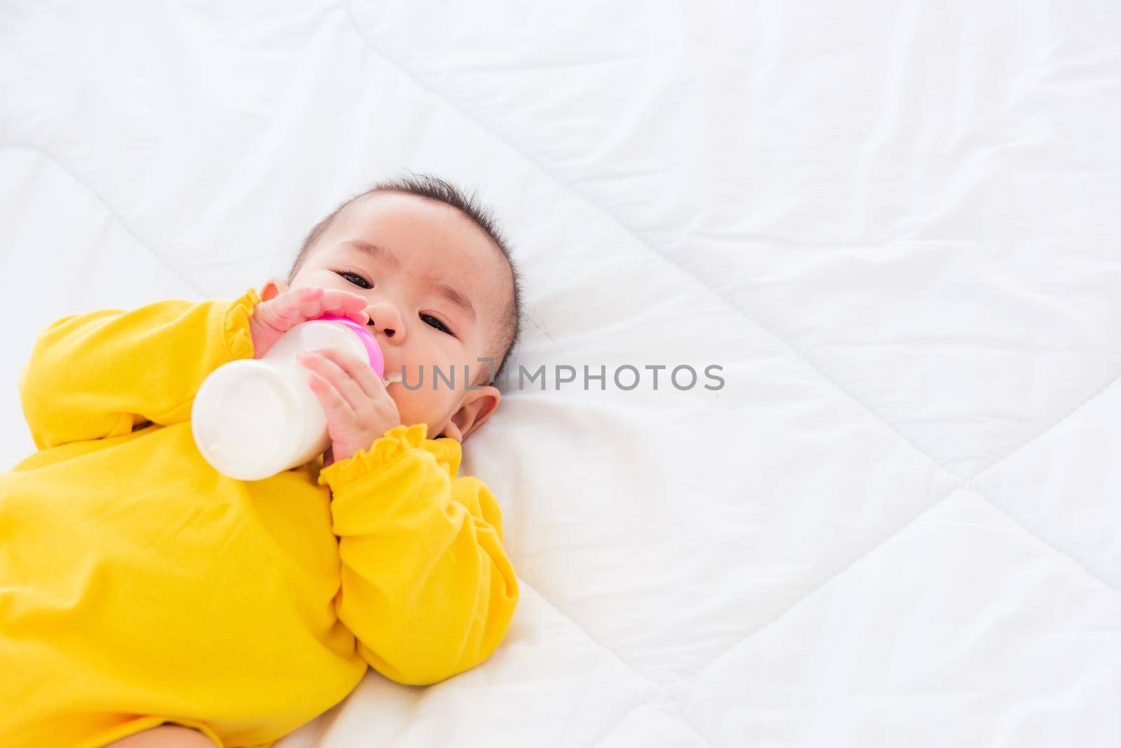 infant holding a bottle of milk by Sorapop