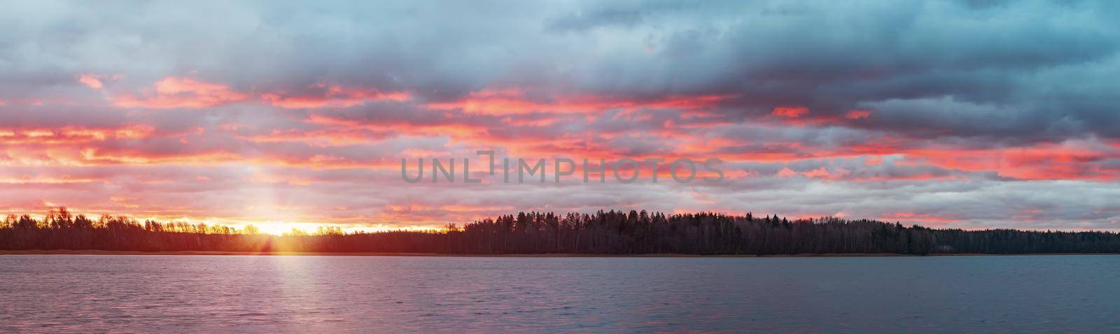 Colorful sunset with dramatic clouds on the lake. Panoramic landscape.