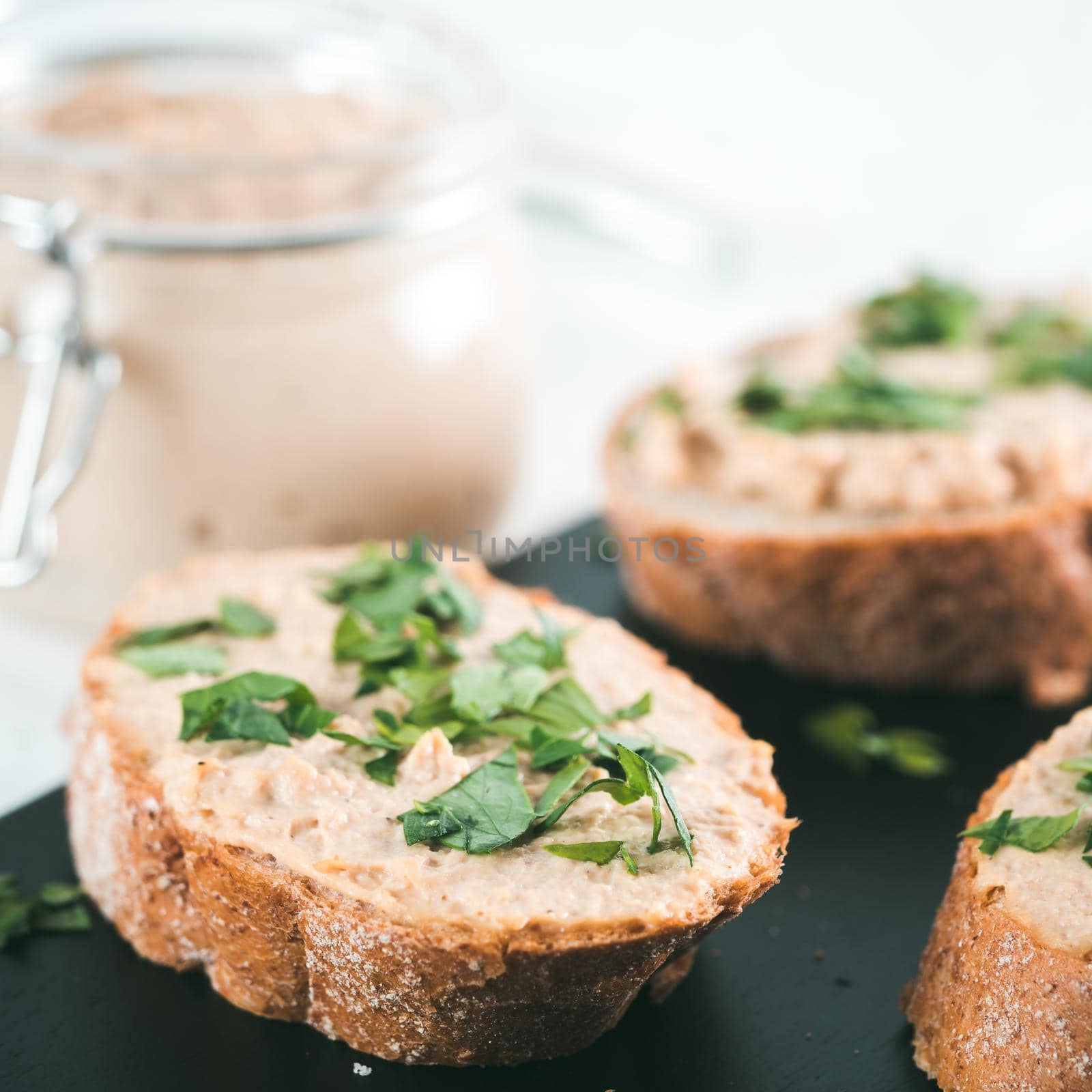 Close up view of slice bread with homemade turkey pate and fresh green parsley on black kutting board over white concrete background, Copy space.